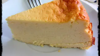 Una rebanada gruesa de tarta de queso cremosa, con la parte superior dorada y un tenedor al fondo.