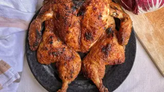 Pollo al horno dorado y crujiente servido en plato negro, acompañado de salsa, limón y col lombarda.