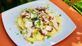 Deliciosa ensalada de pulpo con patatas, cebolla y perejil, servida en un plato blanco sobre un mantel naranja.