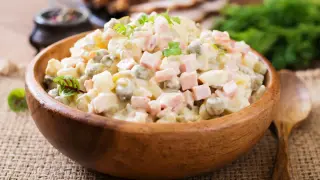 Un cuenco de madera lleno de ensalada alemana, con patatas, guisantes, jamón y un aderezo cremoso.
