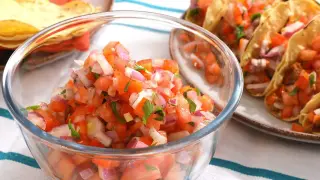 Un tazón de fresco pico de gallo, con tomates picados, cebolla morada y cilantro, listo para acompañar unos tacos.
