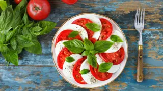 Una deliciosa ensalada caprese con rodajas de tomate y mozzarella fresca, adornada con hojas de albahaca verde vibrante.