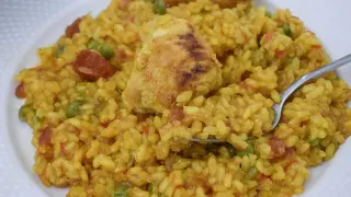 Un plato de arroz con pollo, guisantes y chorizo, con un trozo de pollo dorado encima.