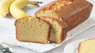 Un delicioso bizcocho de plátano recién horneado, con dos rebanadas cortadas y plátanos amarillos al fondo.