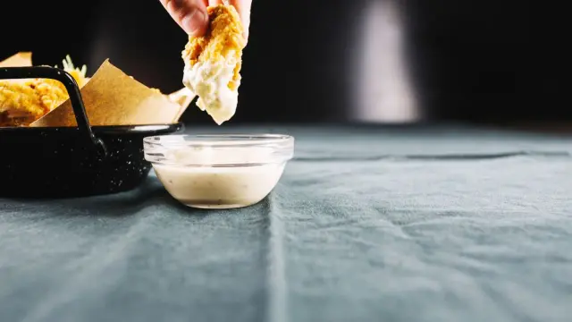 Un trozo de pollo crujiente se sumerge en un cuenco de mayonesa casera, lista para ser disfrutada.