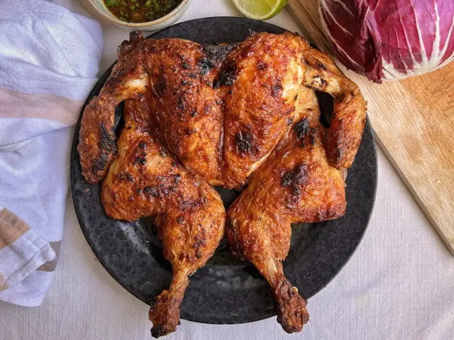 Pollo al horno dorado y crujiente servido en plato negro, acompañado de salsa, limón y col lombarda.