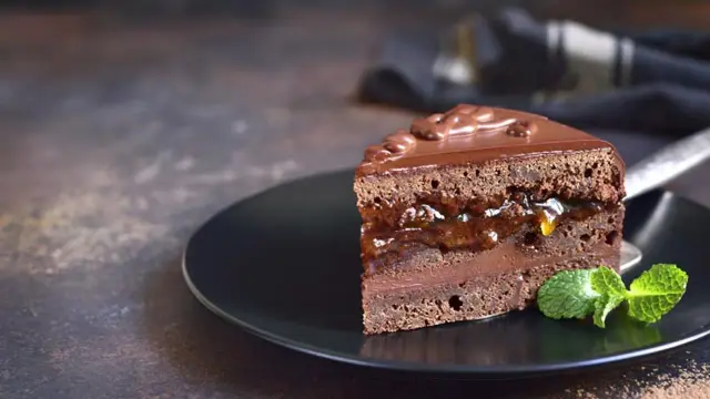 Deliciosa tarta Sacher con doble capa de chocolate y mermelada de albaricoque, cubierta de glaseado brillante y decorada con menta fresca.